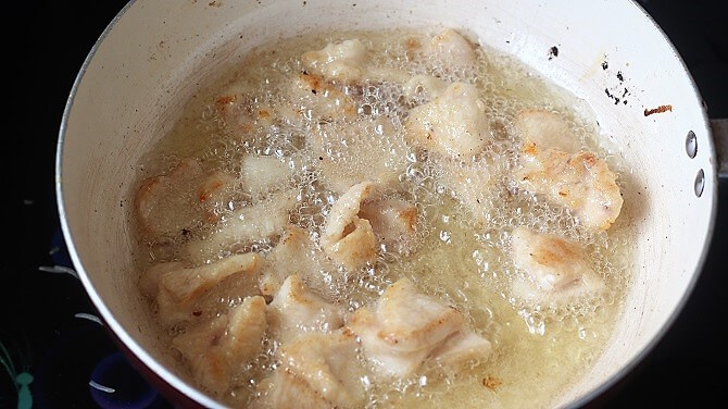 frying chicken in oil in white pan