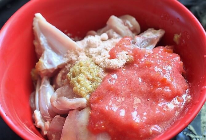 mixing chicken with tomato and ginger garlic paste in a red bowl
